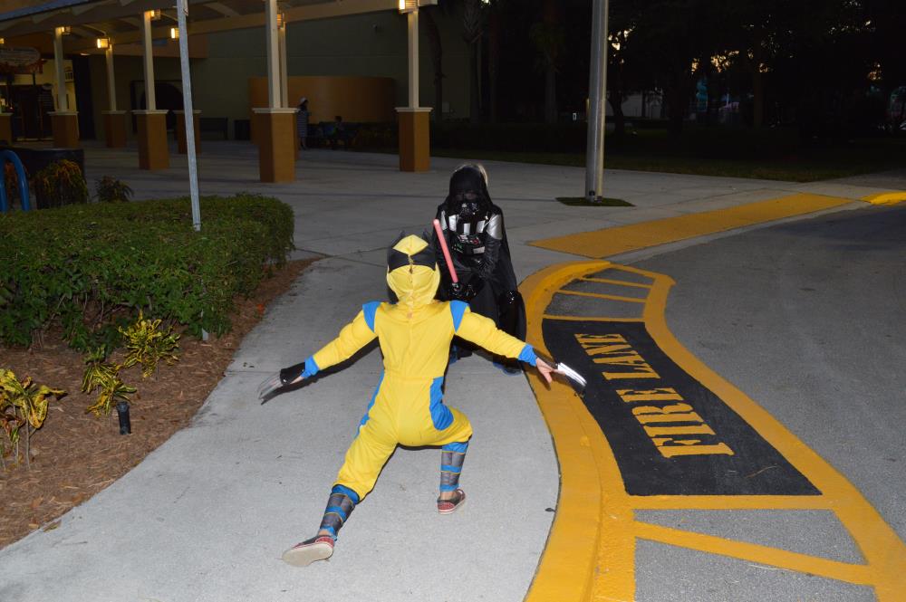 Kid dressed in Darth Vader costume points lightsaber at kid dressed as Wolverine as the two face each other